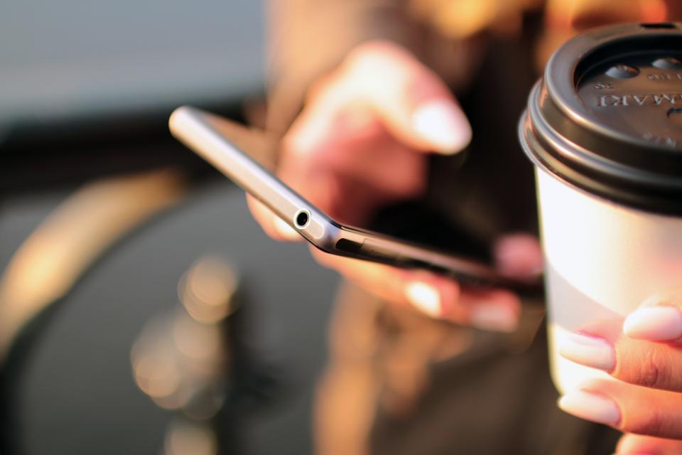 Person holding a smartphone and a coffee cup while scrolling