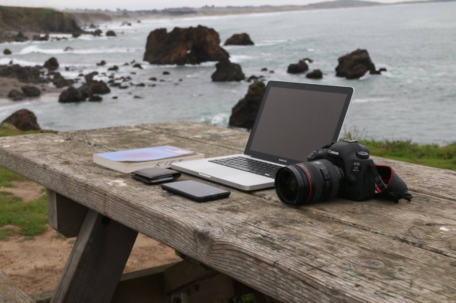Laptop and camera on a wooden table overlooking the ocean