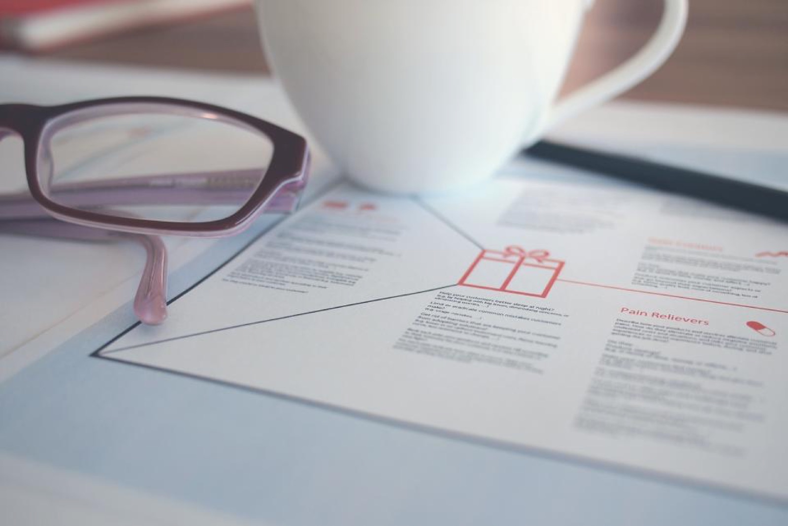 Glasses and a coffee cup on a desk next to a notebook with sketches