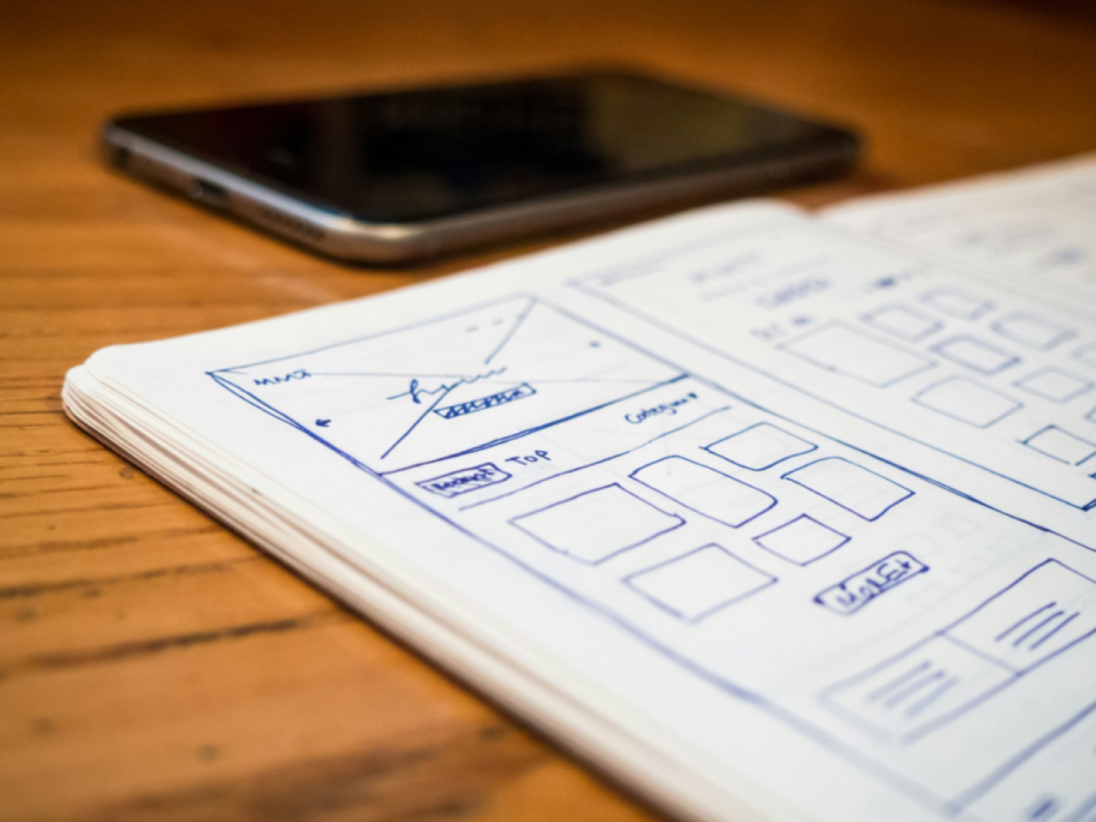 Hand-drawn user interface wireframes on paper next to a smartphone