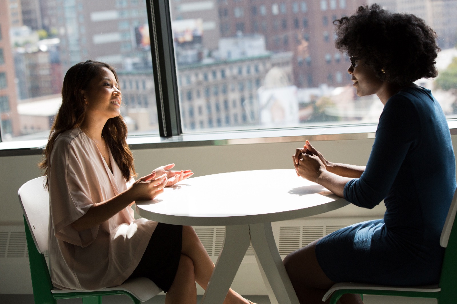 Two businesswomen in conversation at a table by a window