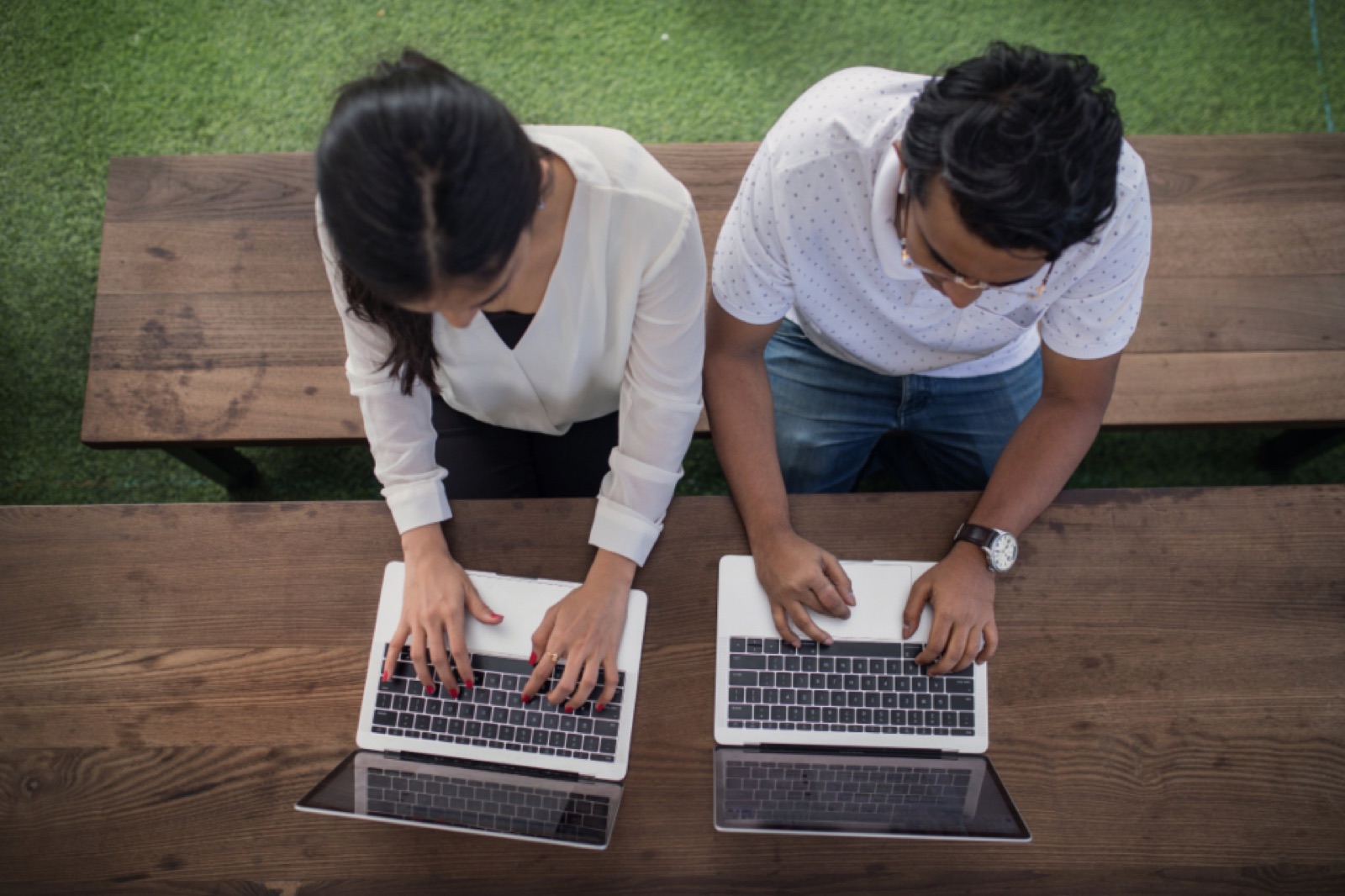 Two coworkers typing on laptops at an outdoor table
