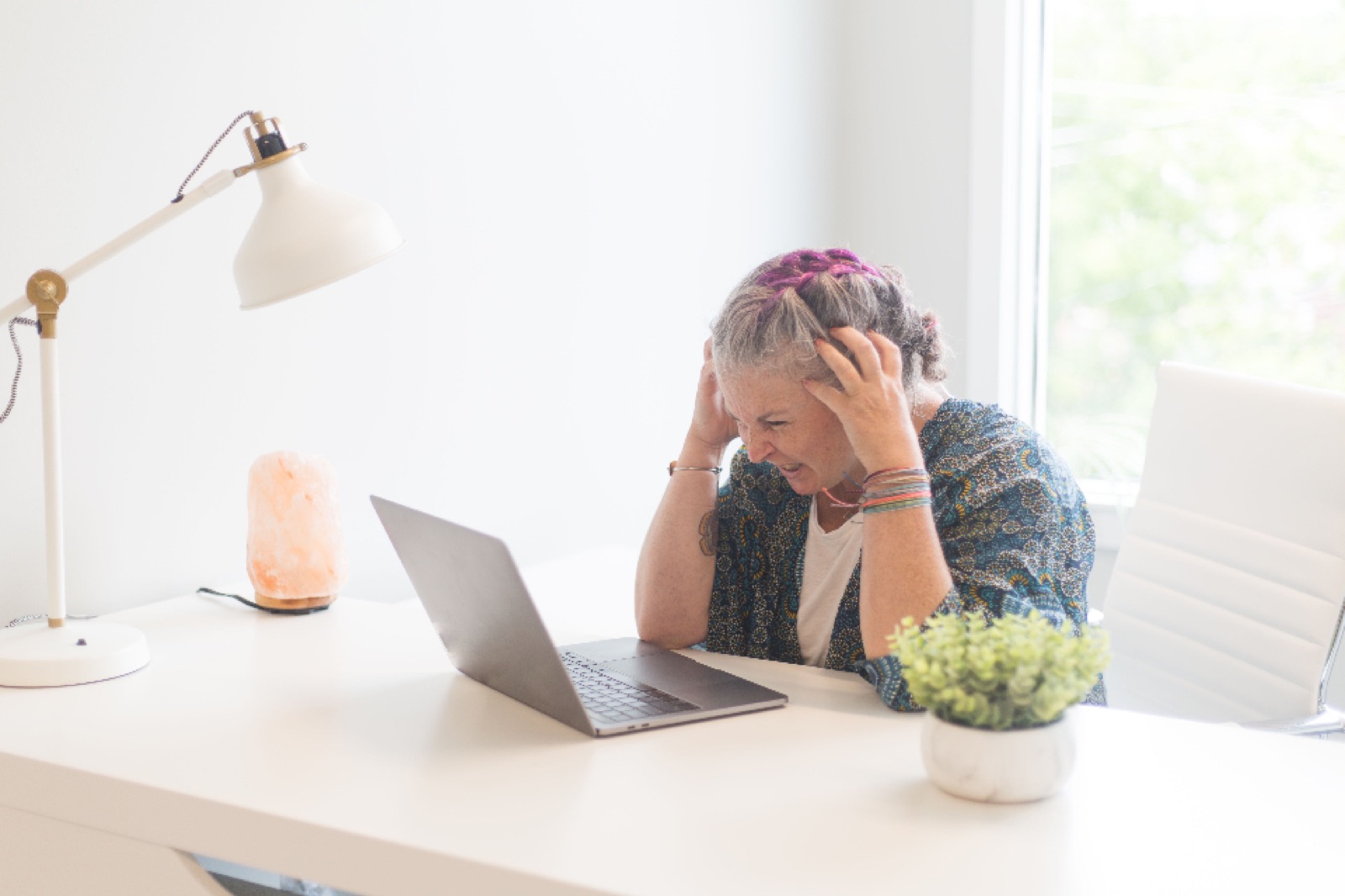 Stressed professional holding her head while working at a laptop