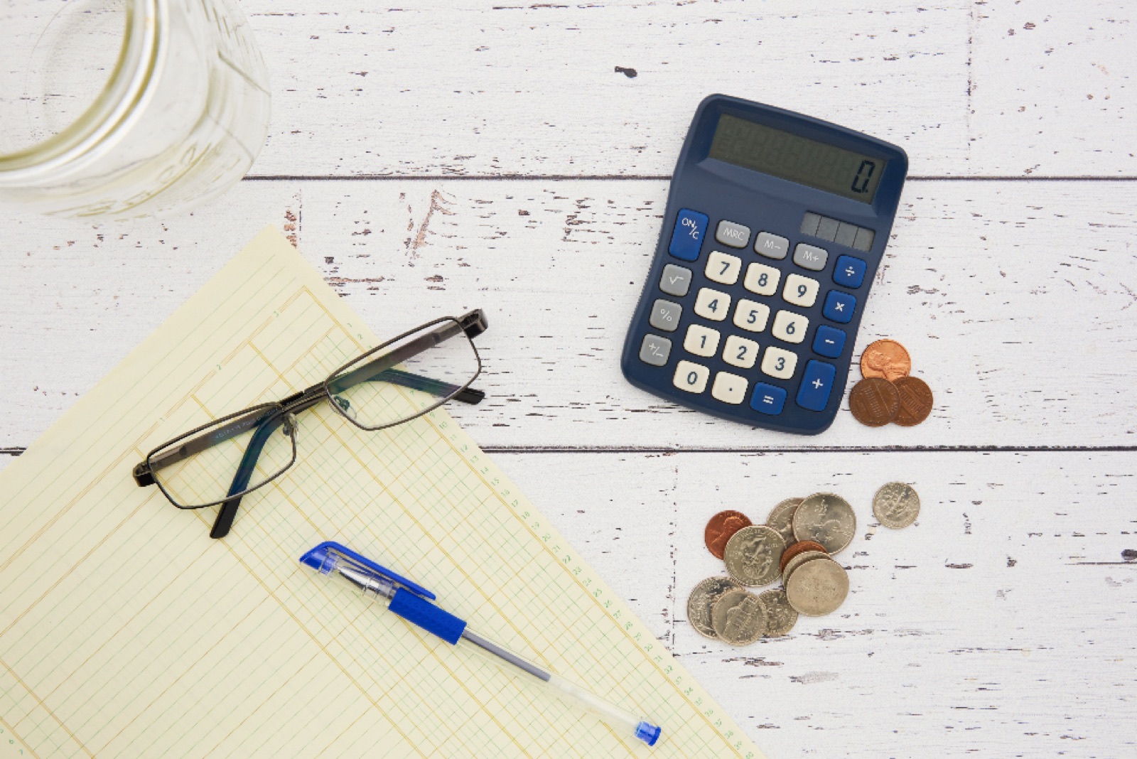 Calculator, coins, glasses and a pen on a notepad