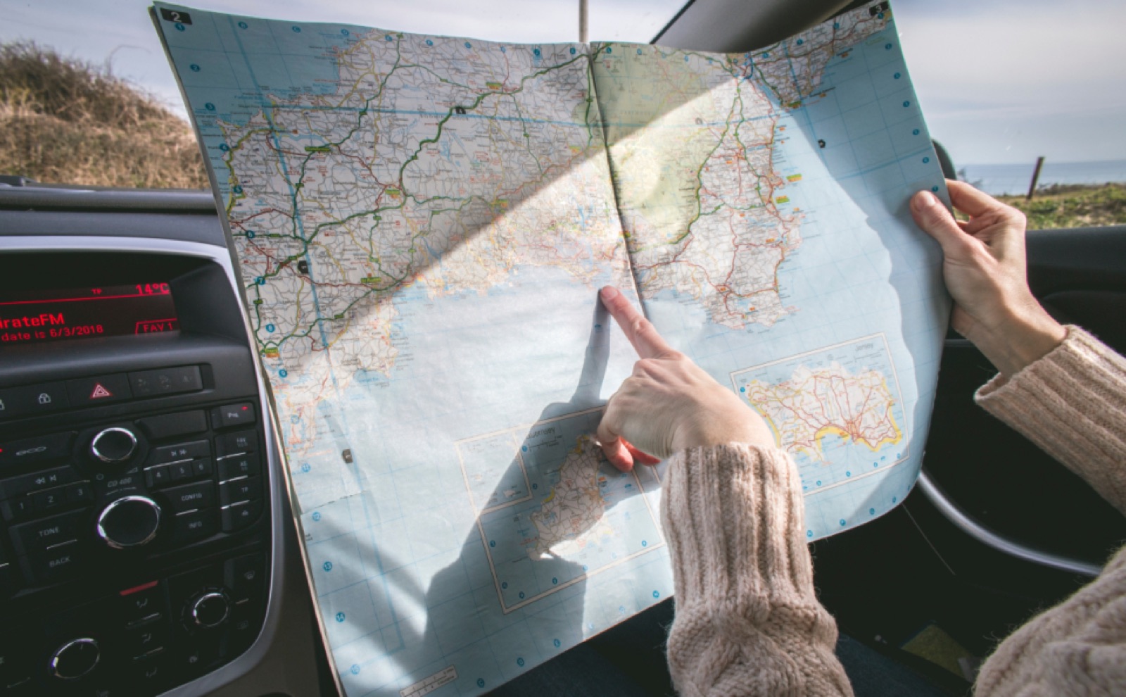Hands holding a road map inside a car